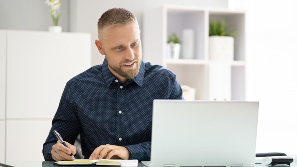 Mężczyzna w trakcie wideokonferencji spisuje ważne punkty w notesie.