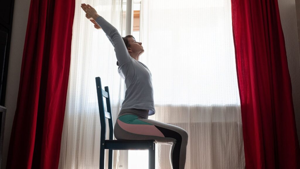 Kobieta siedzi na krześle i rozciąga się, dbając o swoje ciało i dobre samopoczucie.