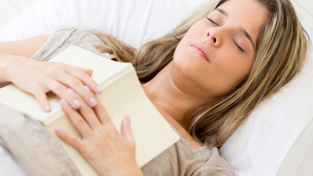 Kobieta zasnęła na kanapie z otwartą książką, ponieważ była zmęczona po pracy.