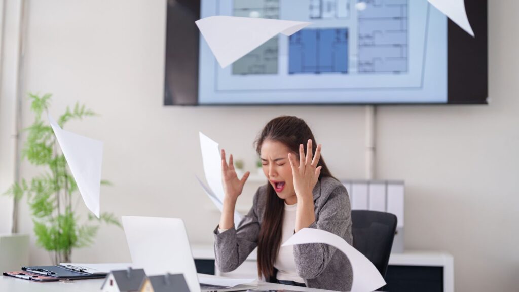 Wściekła kobieta rozrzuca papiery w pracy, ponieważ zauważyła poważny błąd w raporcie, który może mieć konsekwencje dla jej zespołu.