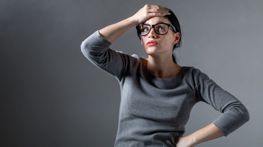 Zmartwiona kobieta trzyma dłoń na głowie i myśli nad rozwiązaniem problemu.