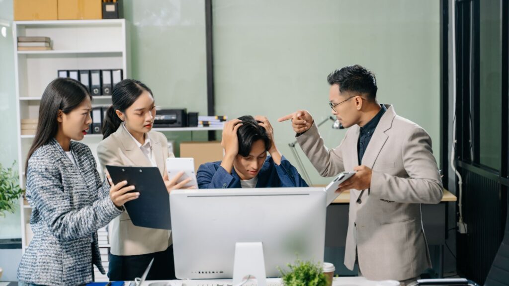 Mężczyzna łapie się za głowę, ponieważ jest przepracowany i dodatkowo ma nałożonych jeszcze więcej obowiązków od współpracowników.