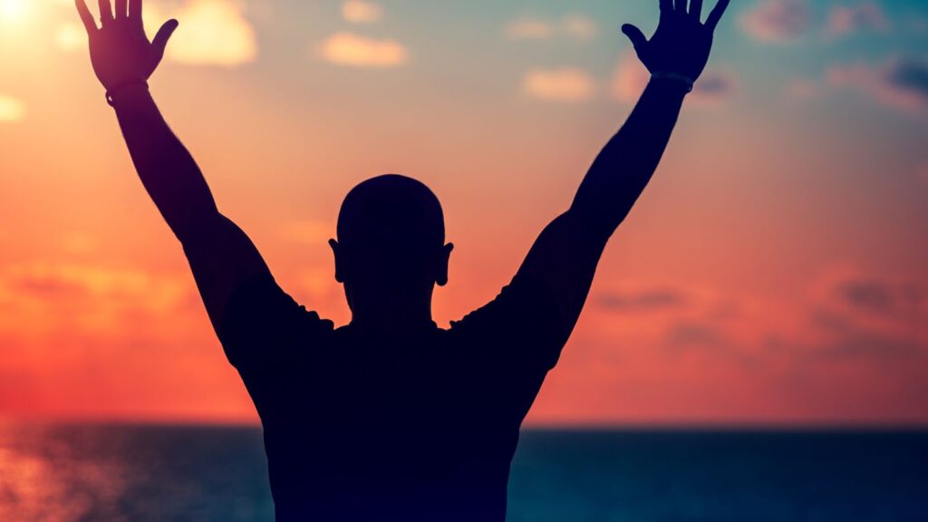 Mężczyzna cieszy się zachodem słońca z rękami uniesionymi ku niebu.