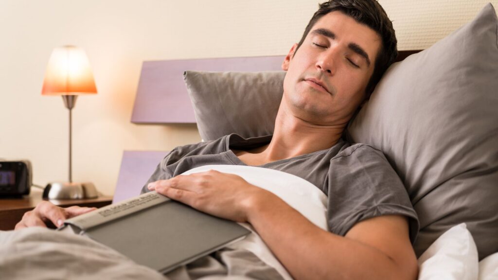 Mężczyzna który cały dzień pracował, zasnął z książką na łóżku.