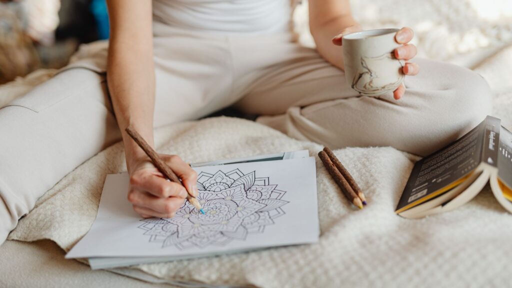 Kobieta relaksuje się po pracy z książką oraz kolorowanką antystresową.