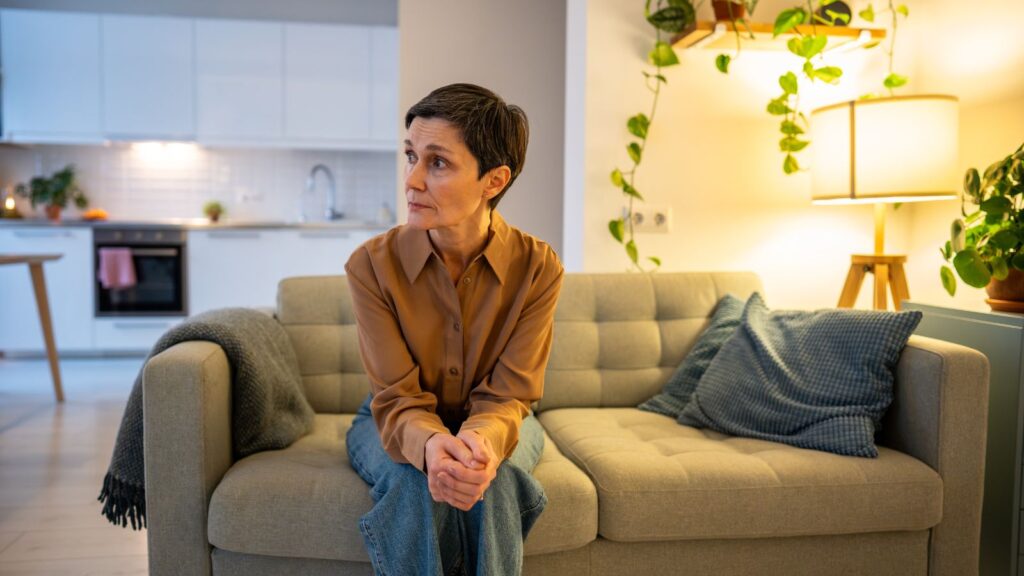 Kobieta siedzi na kanapie i jest w stanie wzmożonego napięcia.