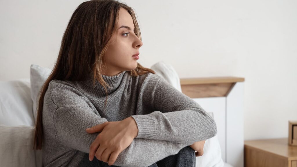 Kobieta w napięciu nerwowym siedzi na łóżku trzymając się za kolana.