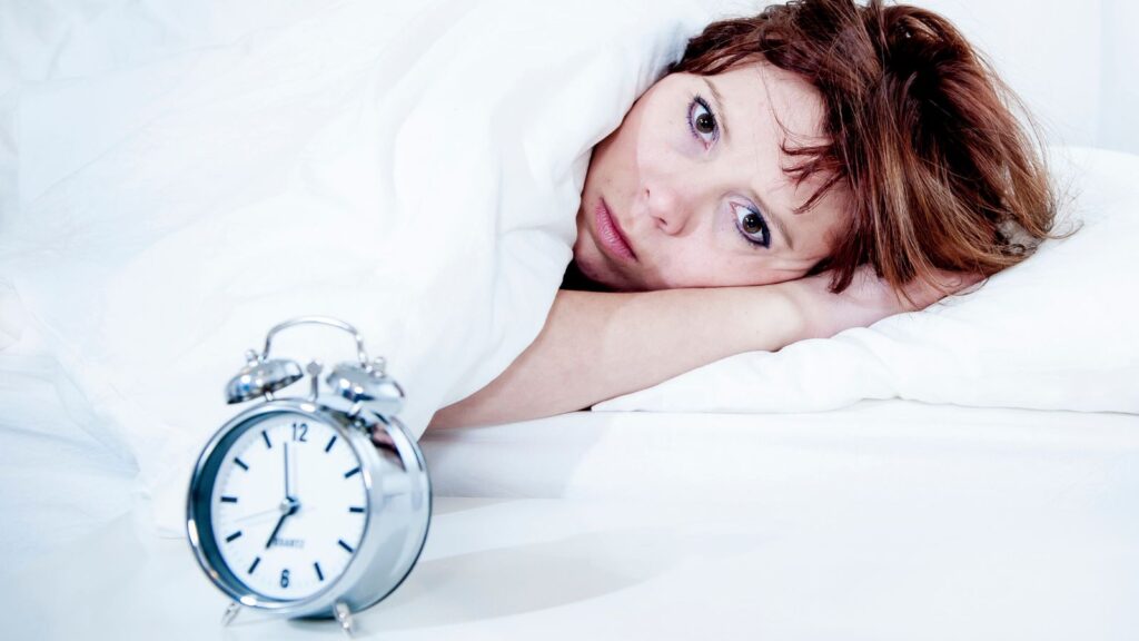 Kobieta leży w łóżku i nie może zasnąć pomimo duzego zmęczenia.