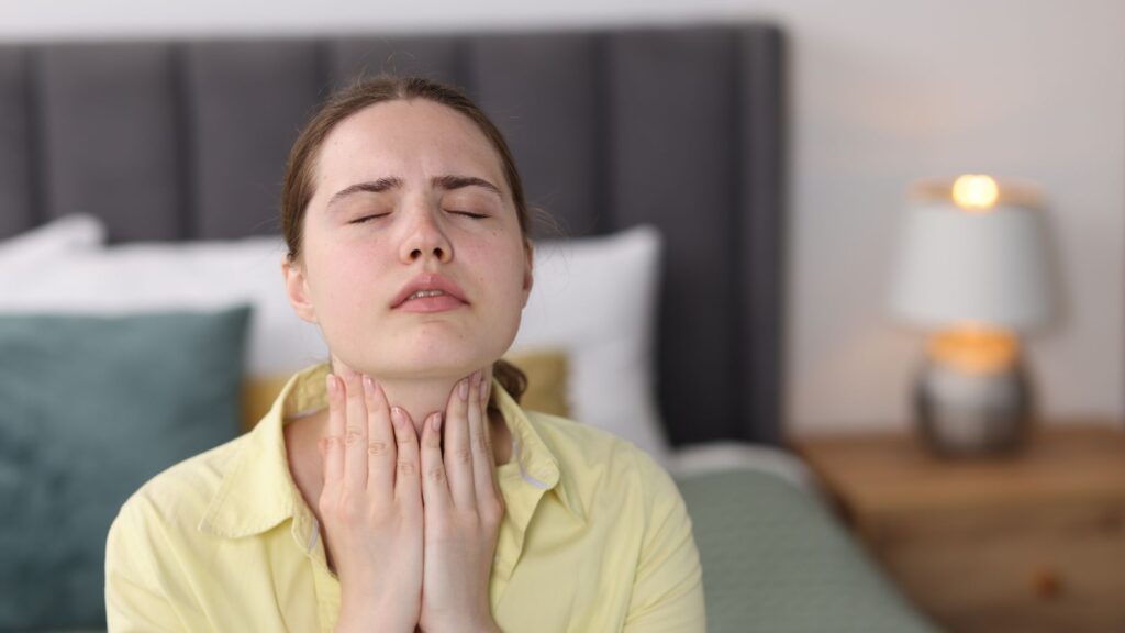 Kobieta o poranku czuje się słabo i trzyma się za szyję, ponieważ jest niewyspana.