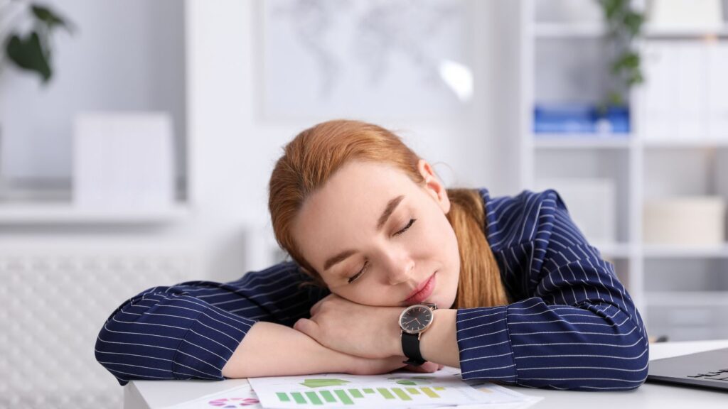 Kobieta w pracy drzemie na biurku, ponieważ jest zmęczona.