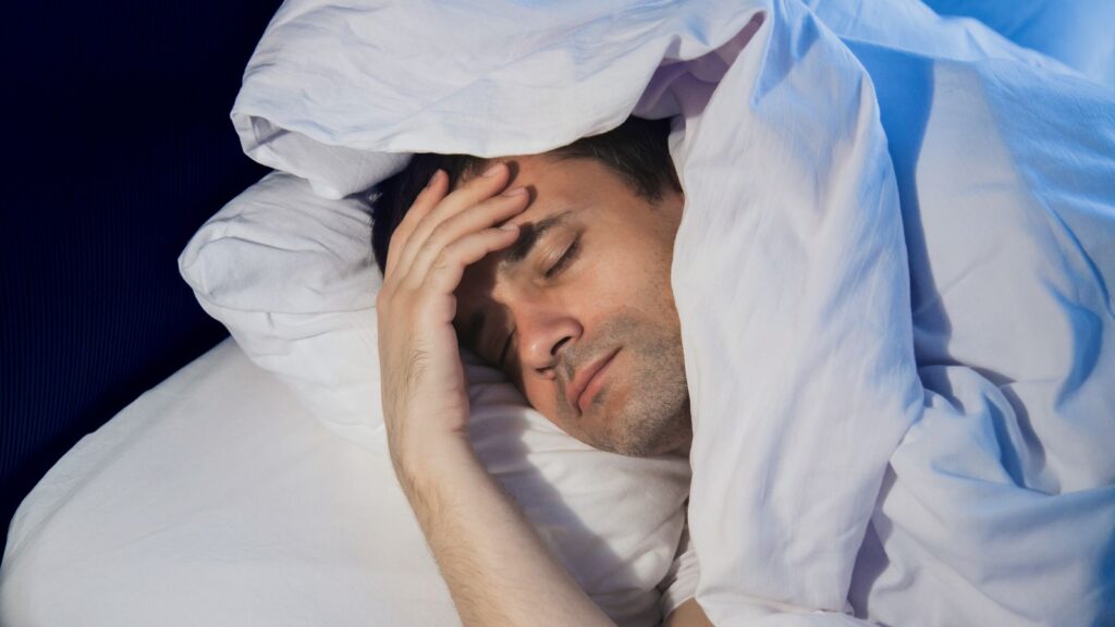 Mężczyzna lezy w łóżku i ma kłopoty z zaśnięciem po pracy.