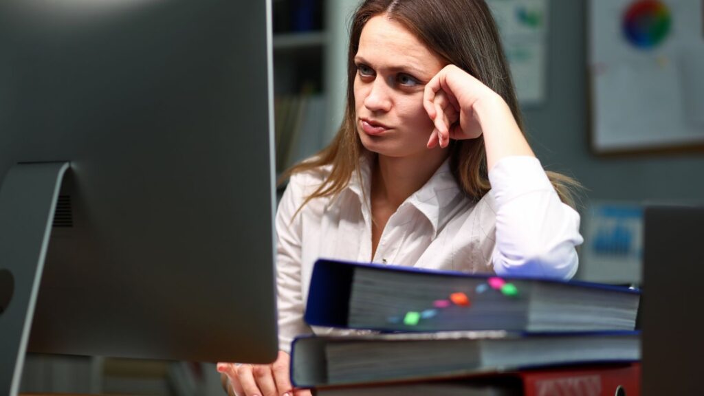 Zmęczona kobieta pracuje przy komputerze, próbując nadążyć za obowiązkami.